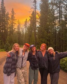 four women posing for a photo in front of the sun setting on a forest trail