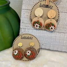 two wooden earrings with flowers on them sitting next to a green vase and white towel