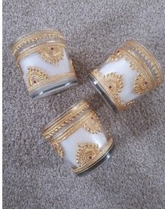 three white and gold glass jars sitting on top of a carpeted floor next to each other