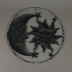 a metal sun and moon decoration hanging on the side of a wall in front of a gray background