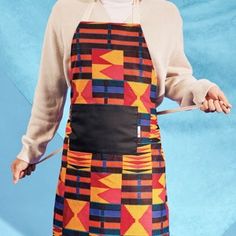 a woman wearing an apron and holding a pair of scissors in one hand while standing against a blue background