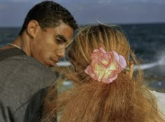 a man and woman standing next to each other near the ocean with flowers in their hair