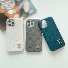 three iphone cases sitting next to each other on top of a white table with a book