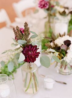 there are flowers in vases on the table with candles and napkins around them