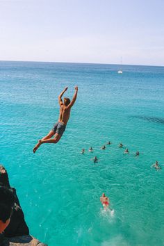 a man is jumping into the water from a cliff in front of other people swimming