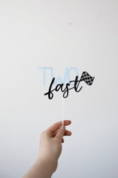 a hand holding a black and white cake topper with the word fast on it