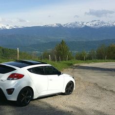 a white car parked on the side of a dirt road in front of snow capped mountains