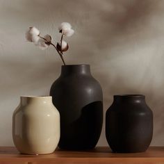 three black and white vases sitting on top of a wooden table next to each other