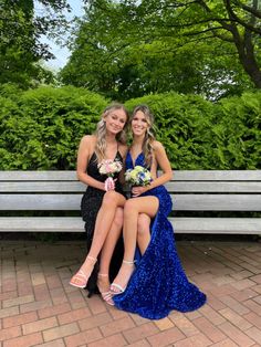 two young women sitting on a bench in front of some bushes and trees, posing for the camera