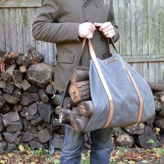 a man holding a bag full of logs in front of a pile of firewood