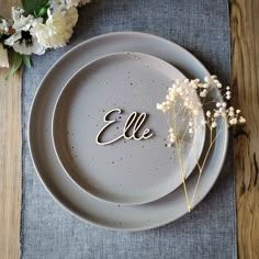 a plate with the word john written on it next to some white flowers and greenery