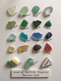 a bunch of different colored sea glass sitting on top of a white table next to a sign