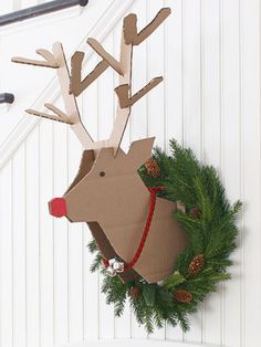 a cardboard reindeer head hanging from the side of a white wall next to a wreath