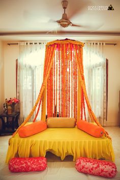 a bed covered in orange and yellow draping next to a window with curtains