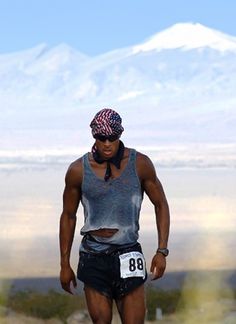 a man standing on top of a snow covered slope wearing shorts and a bandana