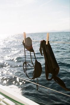 two hats hanging on a rope over the water with sun shining in the distance behind them