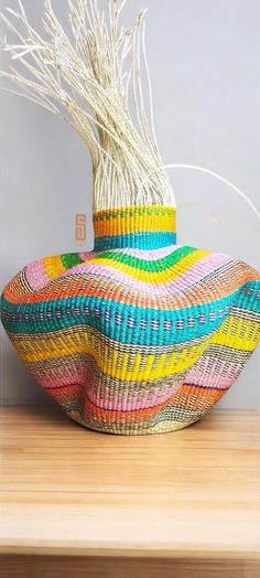 a colorful basket sitting on top of a wooden table next to a vase with dry grass in it