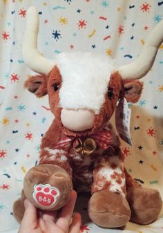 a hand holding a brown and white stuffed cow with horns on it's head