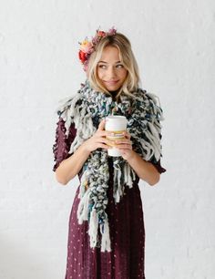 a woman is holding a cup and wearing a scarf