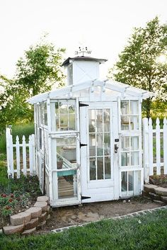 a small white house with an open door and windows on the outside, surrounded by green grass