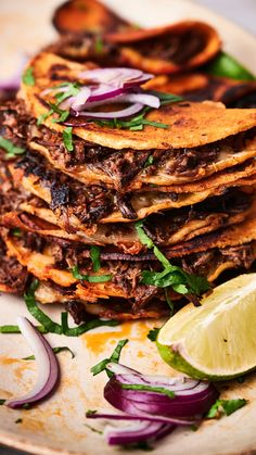 a stack of tortillas on a plate with onions and cilantro wedges