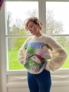 a woman standing in front of a window with her hands on her hips wearing a colorful sweater