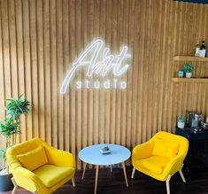 two yellow chairs sitting next to each other in front of a wall with the word alot studio on it