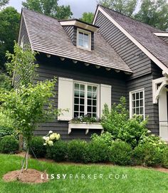 a gray house with white shutters and flowers in the window boxes on the front