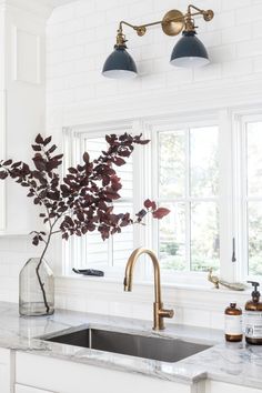 a white kitchen with marble counter tops and brass faucet lighting over the sink