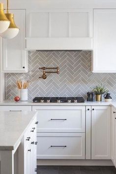 a kitchen with white cabinets and marble counter tops, gold pendant lights over the stove