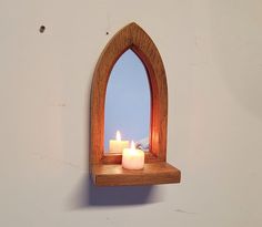 a candle is lit on a shelf with a mirror in the corner and another candle sits next to it