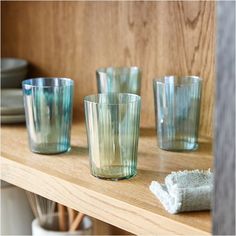 four glass cups sitting on top of a wooden shelf