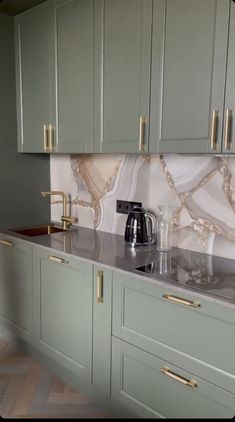 a kitchen with green cabinets and marble counter tops, gold handles on the faucet