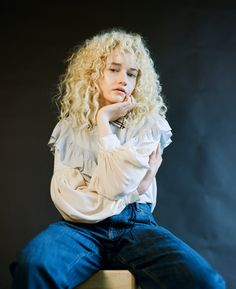 a woman with curly hair sitting on a stool