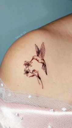 a woman with a hummingbird tattoo on her shoulder and breast is holding a flower