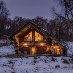 a log cabin in the middle of winter with lights shining on it's windows