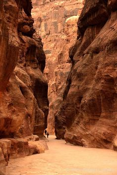 two people are walking through a narrow canyon