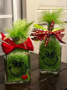 two glass vases with green grass in the shape of grin face and red bow