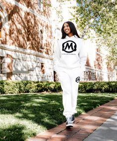 a woman in a white sweatshirt and sweatpants is walking on the sidewalk near a brick building