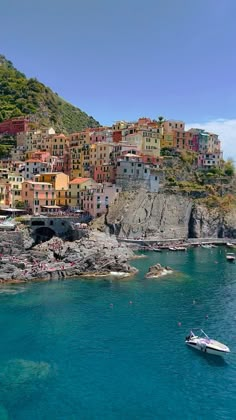 a small boat is in the water near some buildings on a hill side with blue water