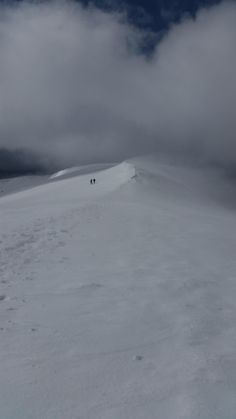 two people walking up the side of a snow covered hill on skis in the distance