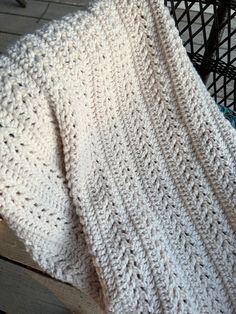 a white knitted blanket sitting on top of a wooden floor next to a basket