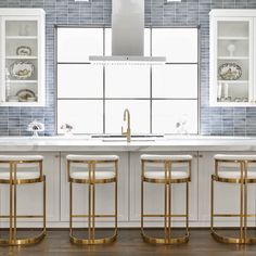 a kitchen with white counter tops and gold barstools in front of a window