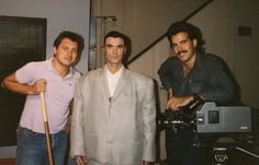 three men standing next to each other in front of a camera and a video camera