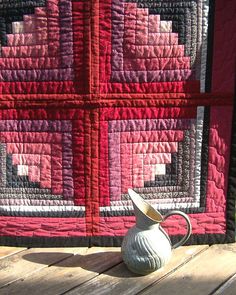 a white vase sitting on top of a wooden table next to a pink and black quilt