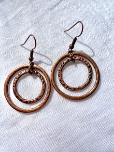 These earrings consist of two different sized hammered copper rings; the smaller ring hanging inside of the larger one. Extremely lightweight and versatile.  These earrings hang on hypoallergenic ear hooks. Artisan Copper Gold Hoop Earrings, Bohemian Copper Earrings With Hammered Detail, Bohemian Copper Spiral Earrings, Unique Nickel-free Copper Hoop Earrings, Artisan Copper Hoop Earrings, Pierced, Hammered Copper Earrings, Copper Rings, Hammered Copper, Ear Hook