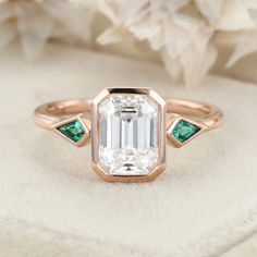 an emerald and diamond engagement ring on top of a white flowered cloth with flowers in the background