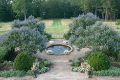 an aerial view of a fountain surrounded by trees and shrubs in the middle of a garden