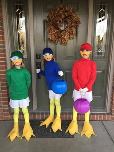 three children in duck costumes are standing on the front porch with balloons and rubber ducks