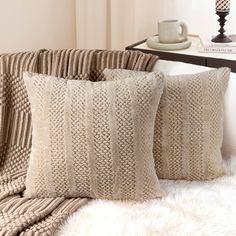 two pillows sitting on top of a bed next to a white fur covered table and chair